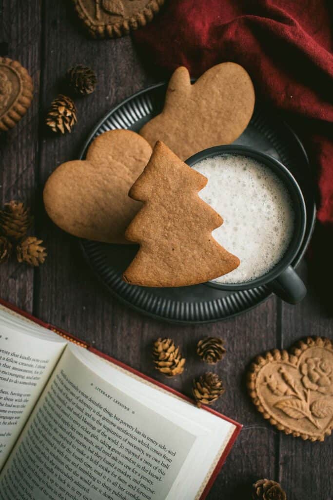 Brown cut-out cookies on and around a mug filled with a frothy drink.