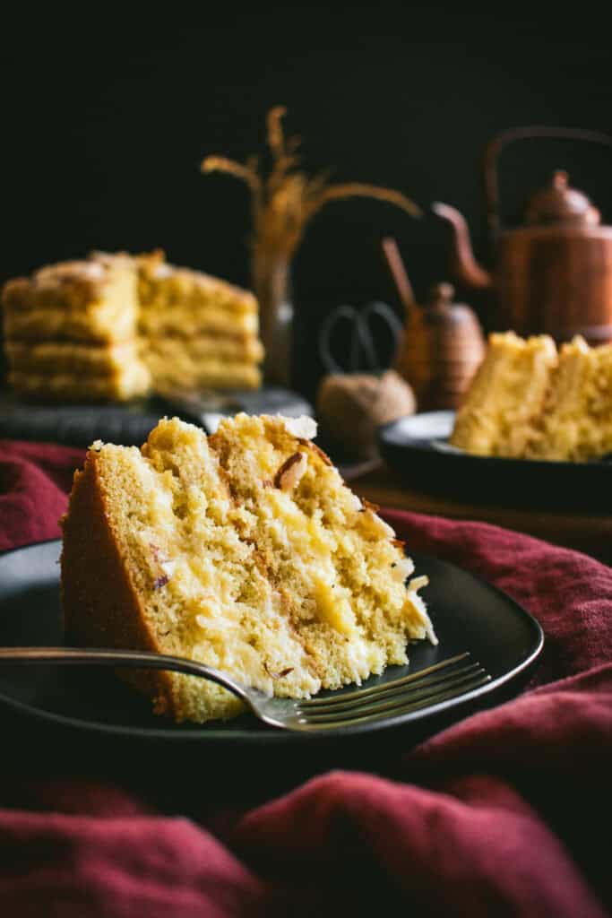 Slices of four-layer almond cake with a creamy filling on small black plates on a dark red linen.