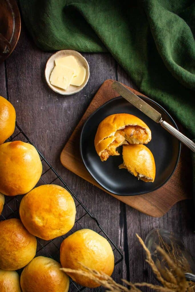 A soft bread roll cut in half to show caramelized onions and melted cheese inside, resting on a black plate.