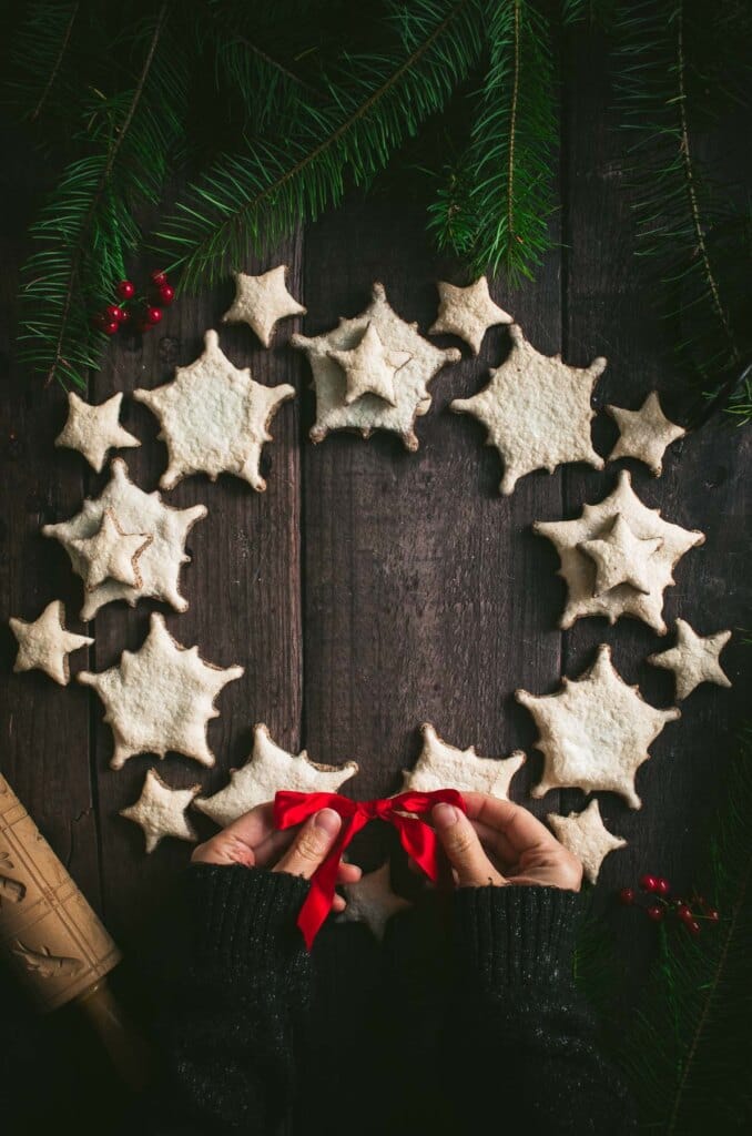 Two hands tying a red ribbon on top of a ring of star shaped cookies.
