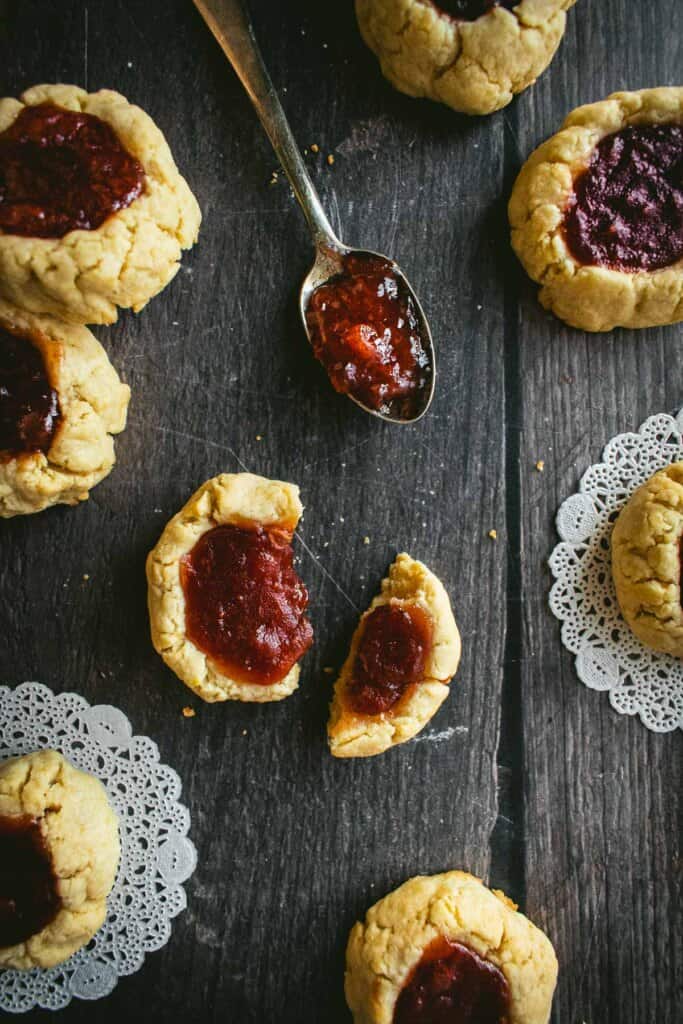 A spoon with jam next to jam thumbprint cookies.