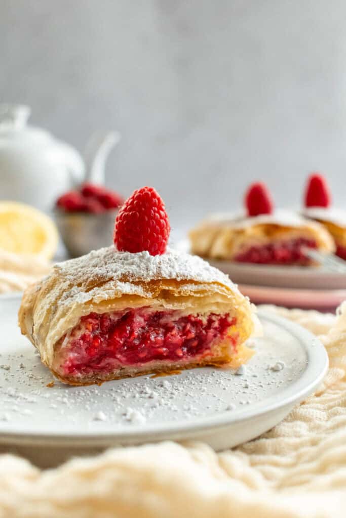 Slices of flaky raspberry strudel on grey plates topped with powdered sugar and fresh raspberries.