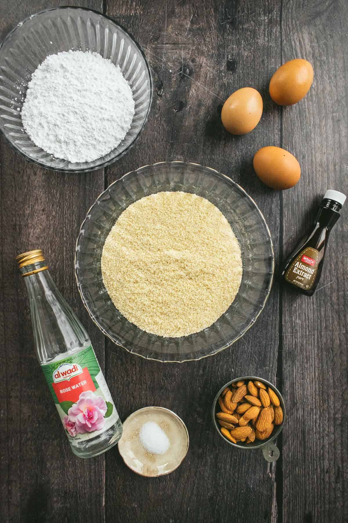 Bowls of almond flour and powdered sugar next to eggs, almonds, salt, and rose water.