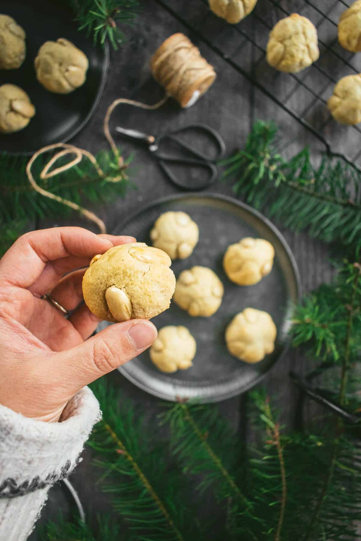 A hand holding a small German marzipan cookie with blanched almonds pressed into the sides.