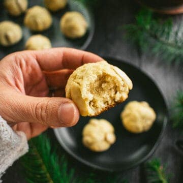 A hand holding a small light cookie with a bite taken out of it.