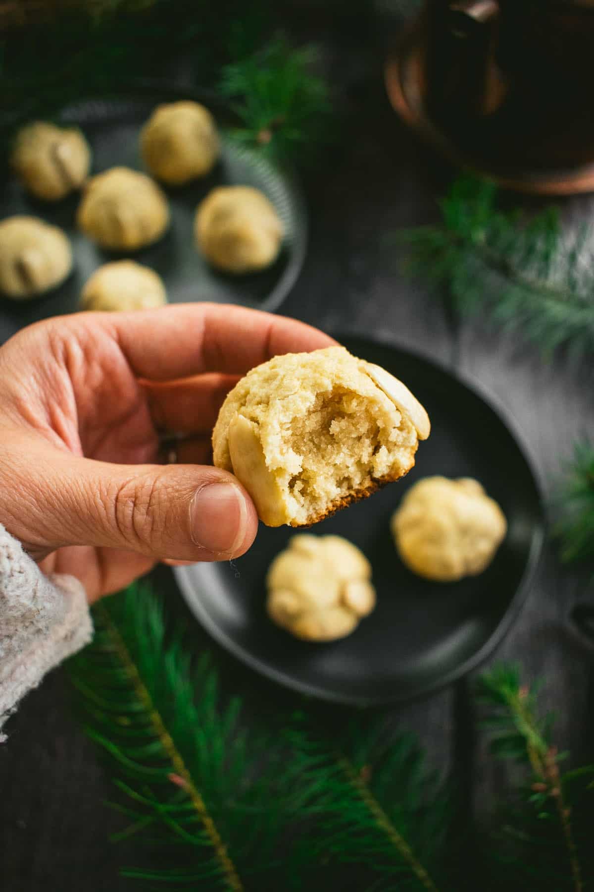 A hand holding a small light cookie with a bite taken out of it.