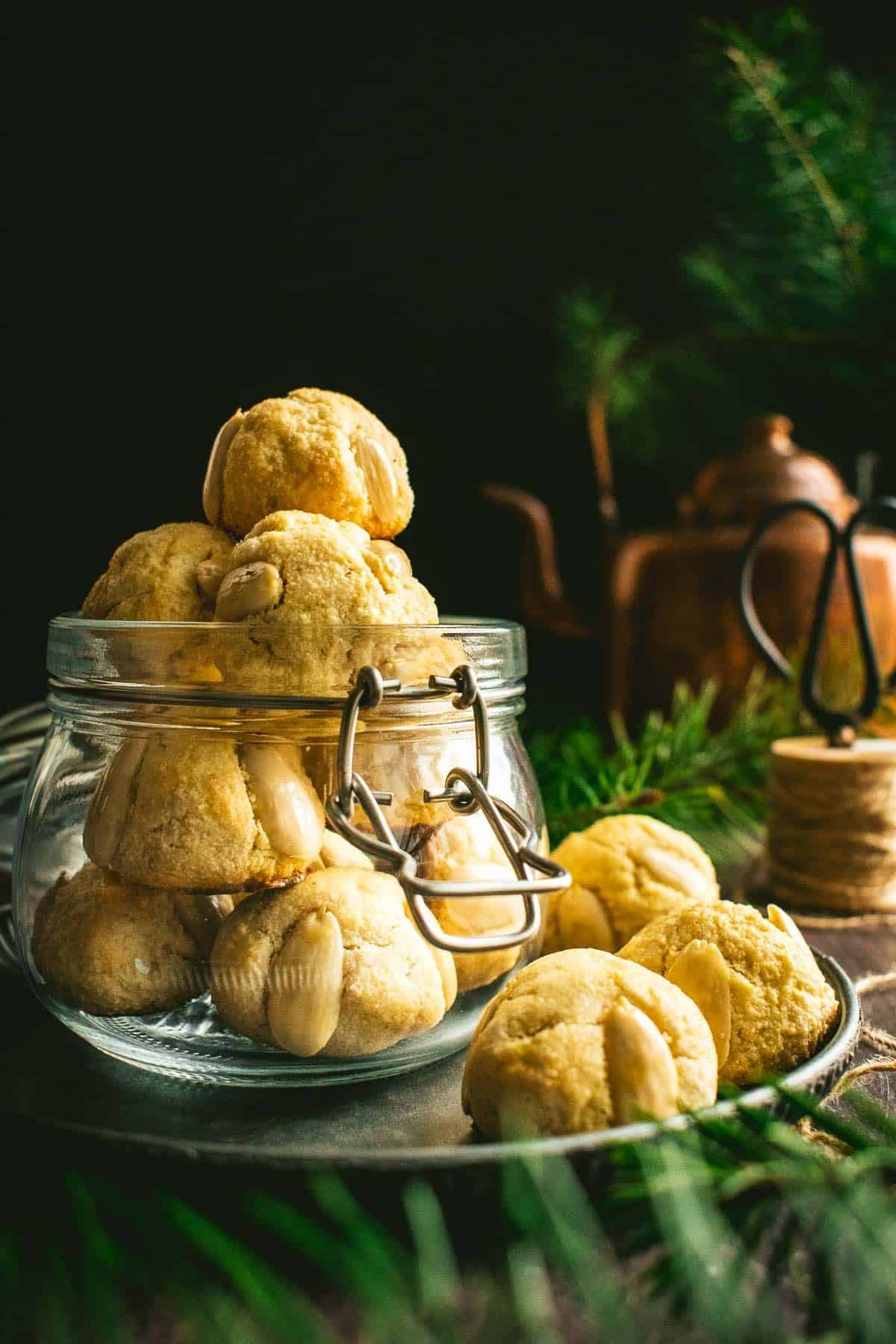 A glass jar filled with small German cookies with blanched almonds on the sides.