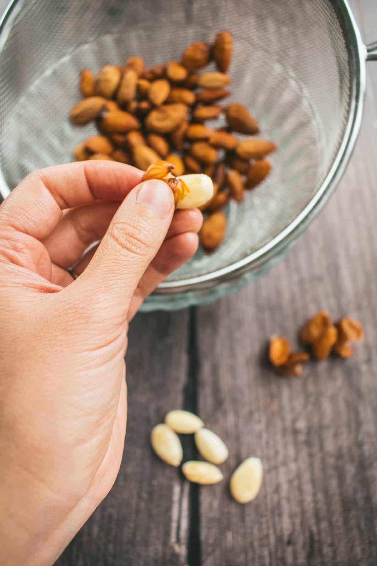 A hand squeezing a whole almond out of its skin.