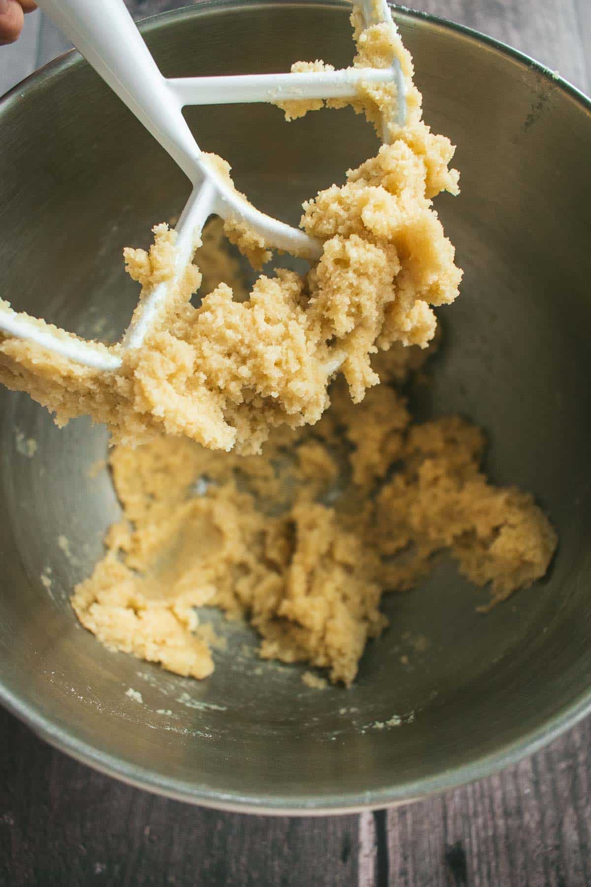 A stand mixer paddle attachment covered in a light, sticky cookie dough.