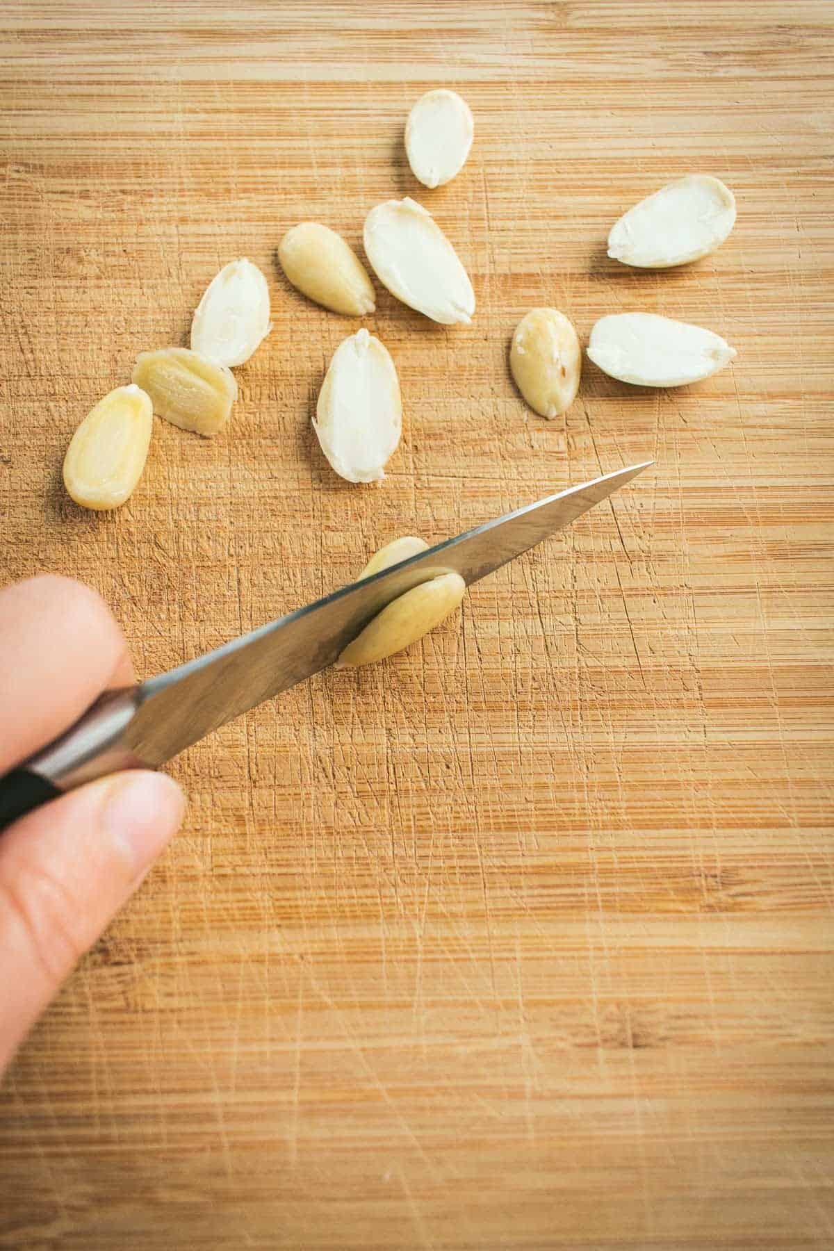 A knife cutting a blanched almond in half length-wise.