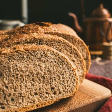 Two slices of dark brown wheat bread leaning against the rest of the loaf on a wood board.