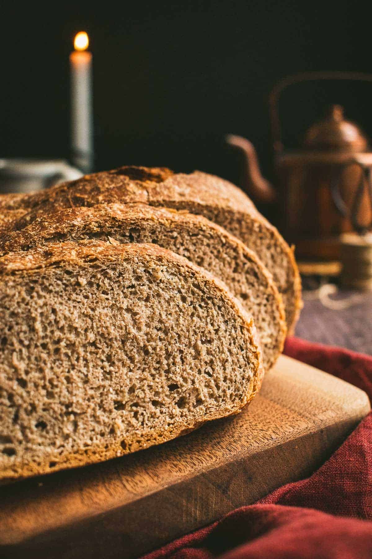 Two slices of dark brown wheat bread leaning against the rest of the loaf on a wood board.