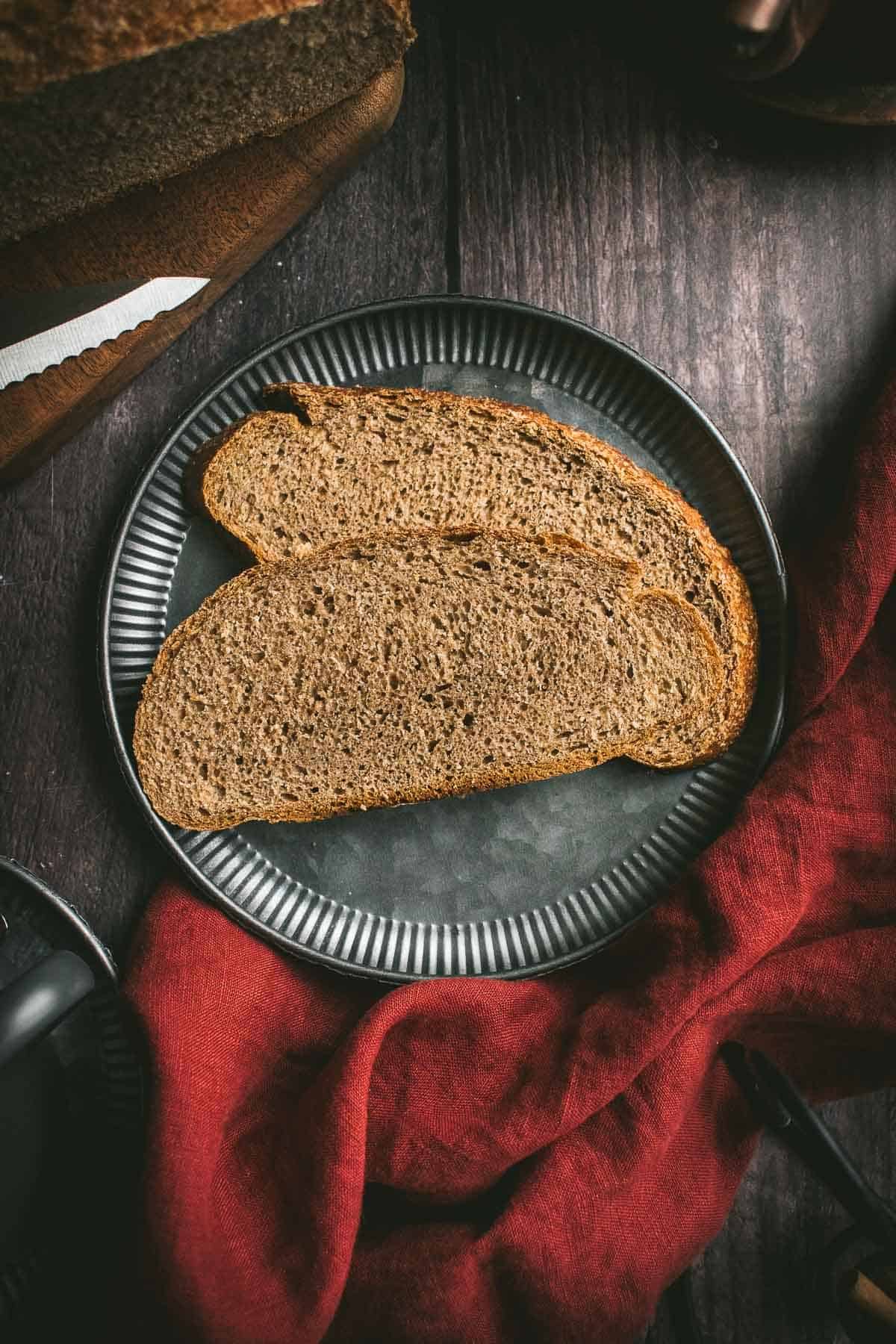 Two slices of dark brown wheat bread on a metal plate on a wooden table.