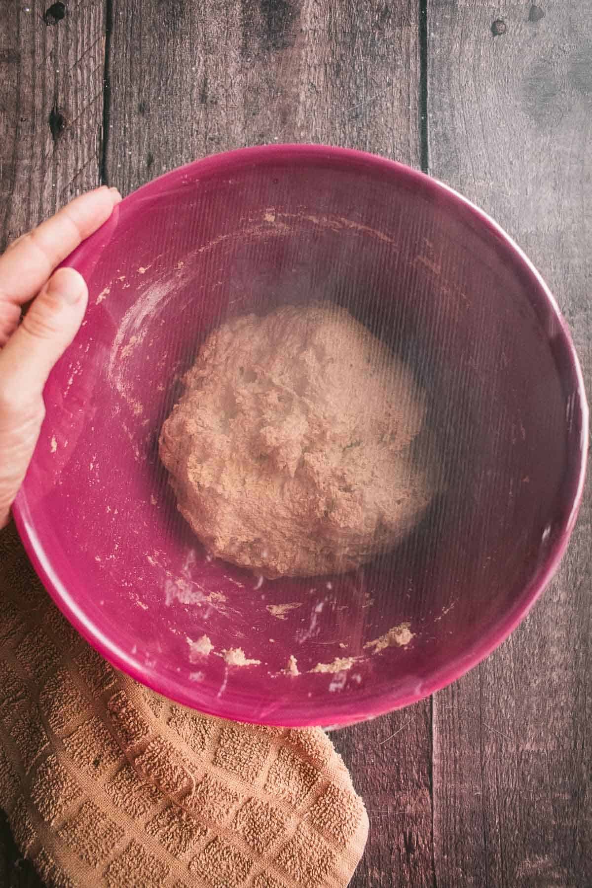 Wet bread dough in a mixing bowl covered with plastic wrap.