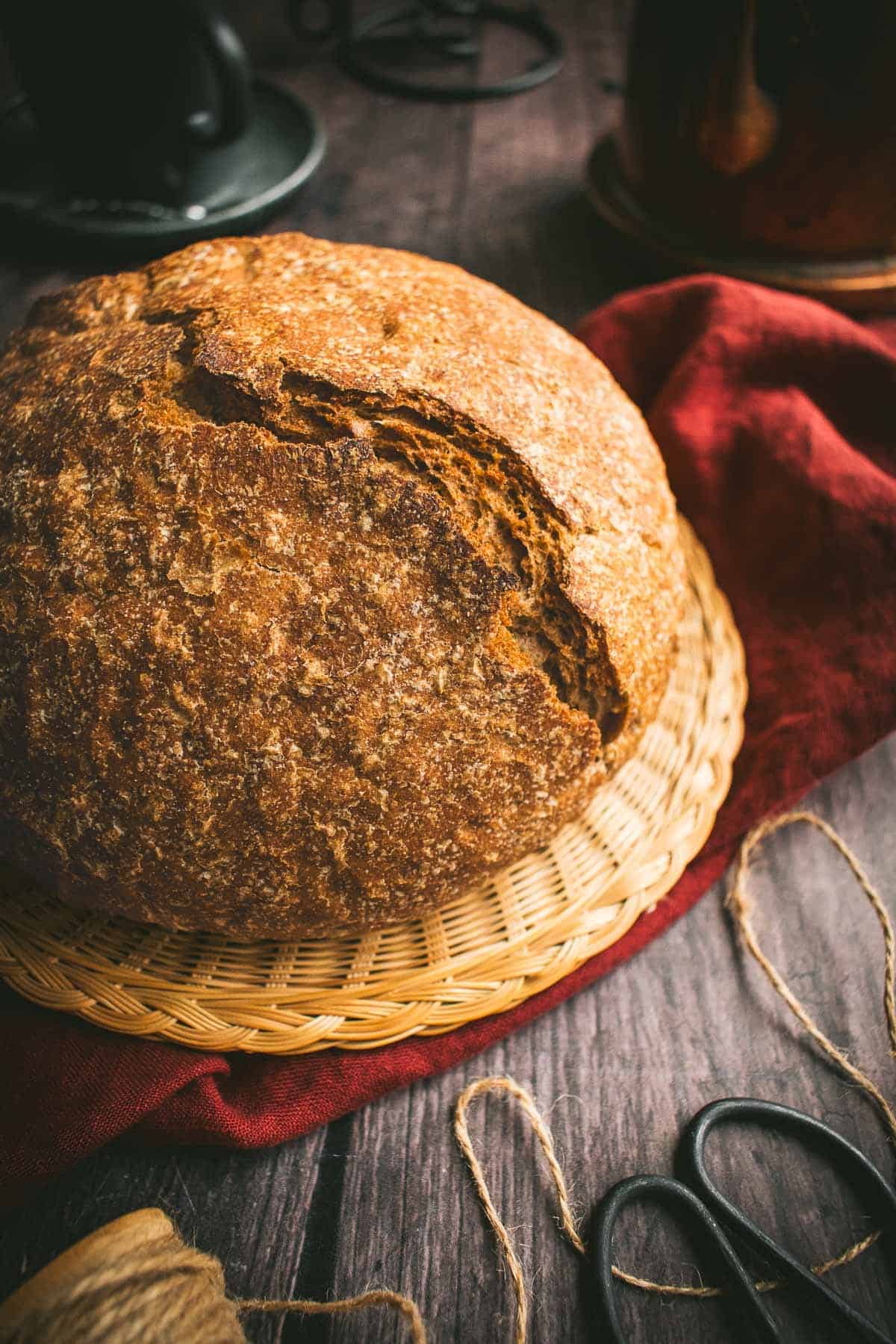 A round loaf of whole wheat bread with a crispy crust on a wicker trivet.