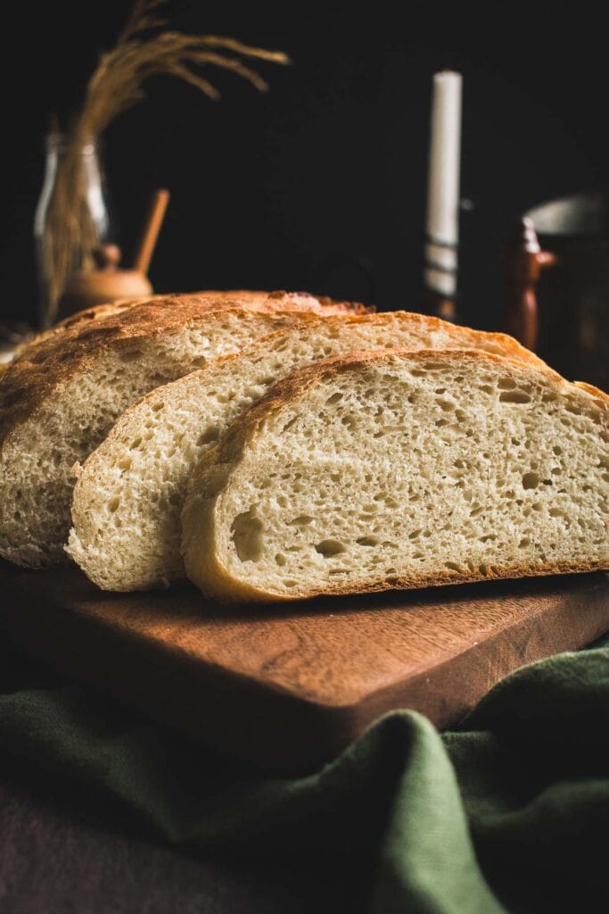 Two thick slices of white bread on a cutting board leaning on the rest of the loaf.