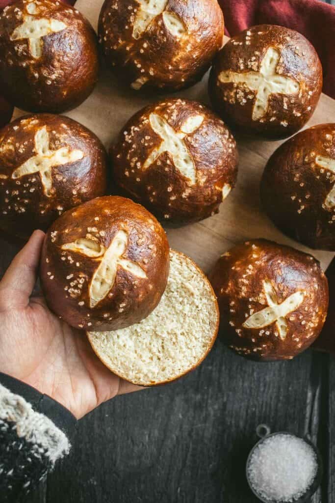 A hand holding a dark brown pretzel bun cut in half.