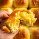 A half-eaten fluffy dinner roll with melted cheese inside.