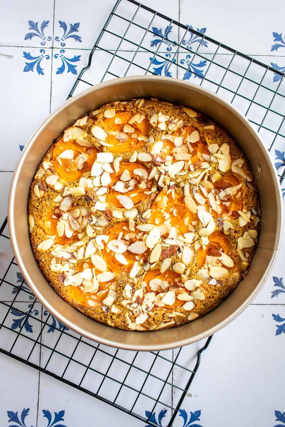 An apricot cake covered in almonds on a cooling rack. 