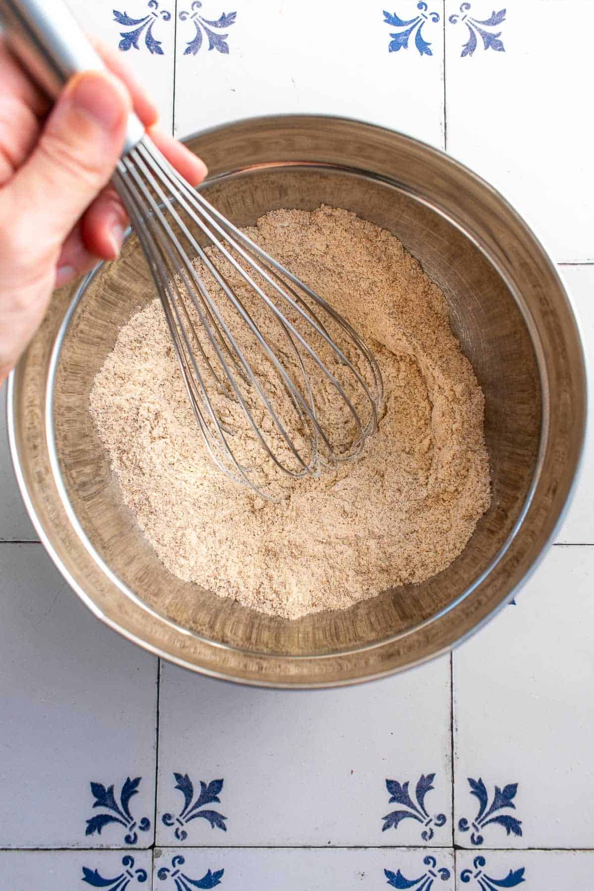 A hand whisking almond flour and flour in a bowl. 