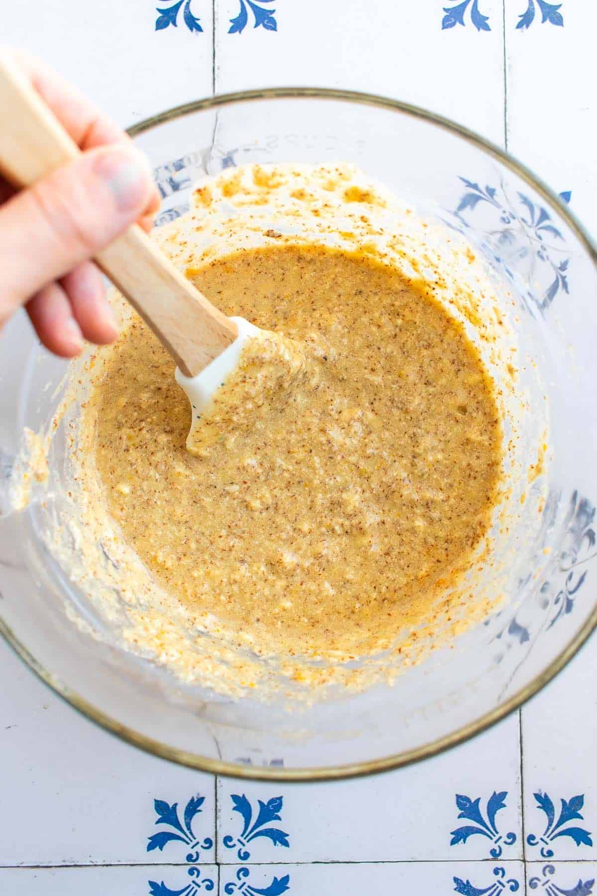 A hand stirring almond cake batter in a bowl. 