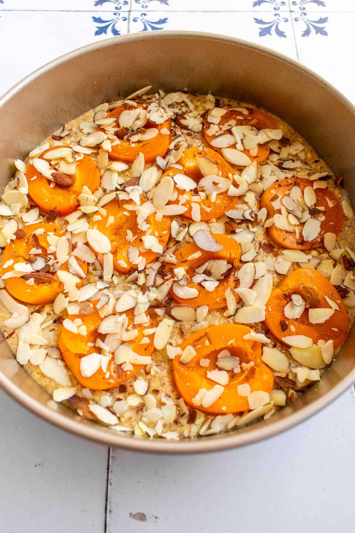 Halved apricots and sliced almonds on top of cake batter in a cake pan.