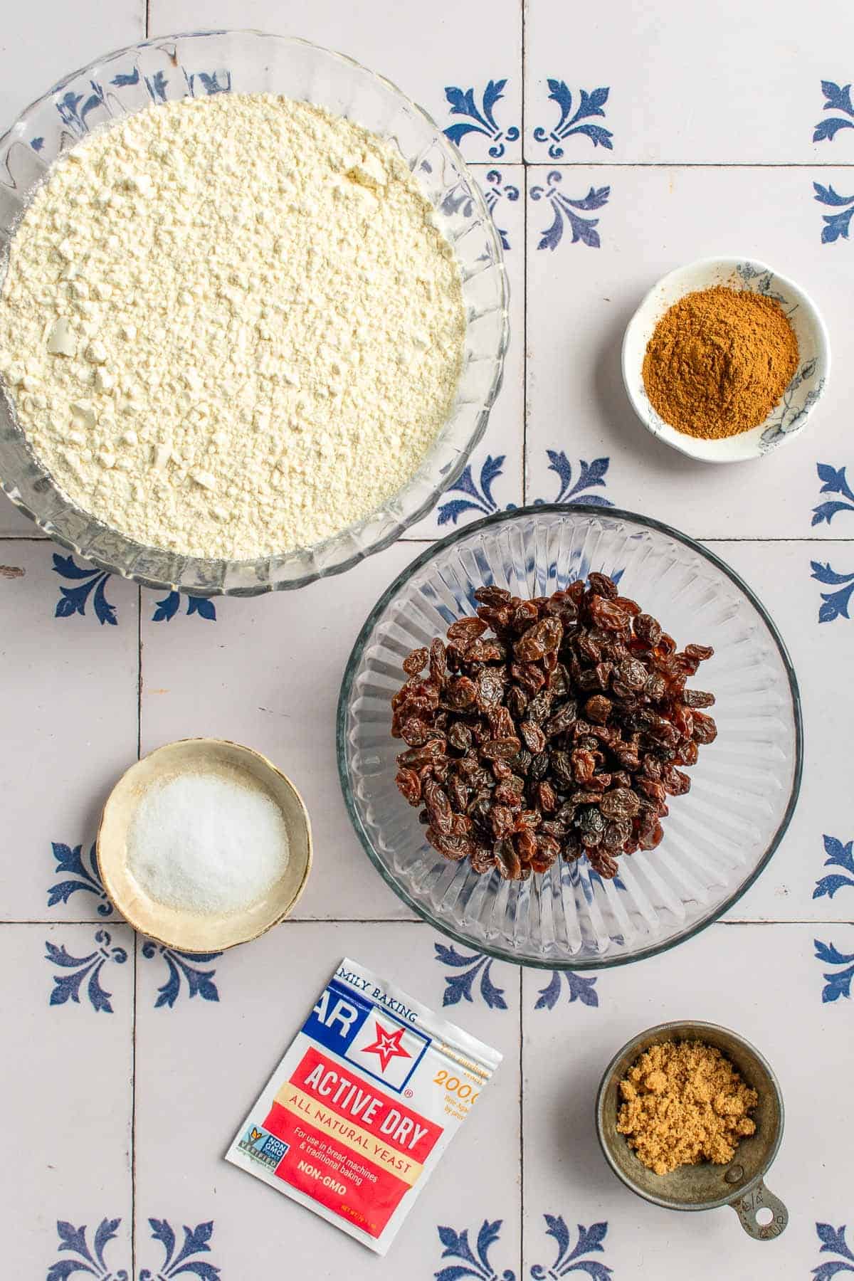 Bowls of raisins, brown sugar, flour, salt, and cinnamon next to a packet of yeast.