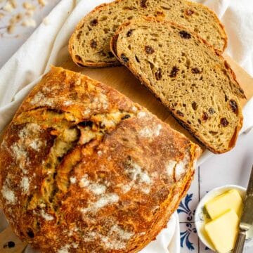 Two slices of bread filled with raisins next to a crusty loaf.