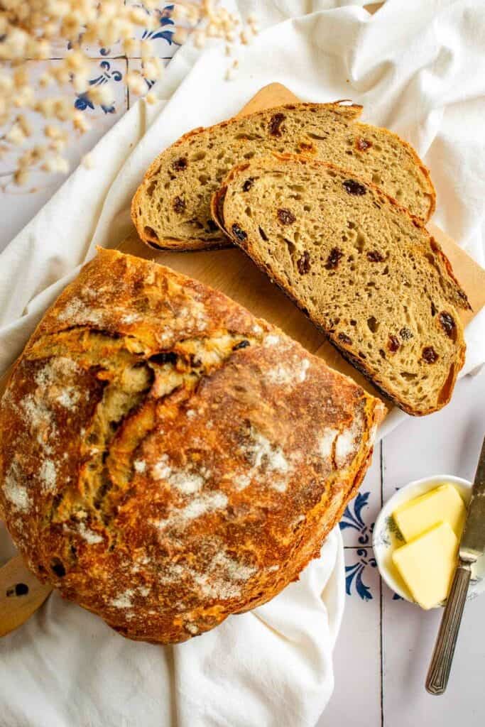 Two slices of bread filled with raisins next to a crusty loaf.