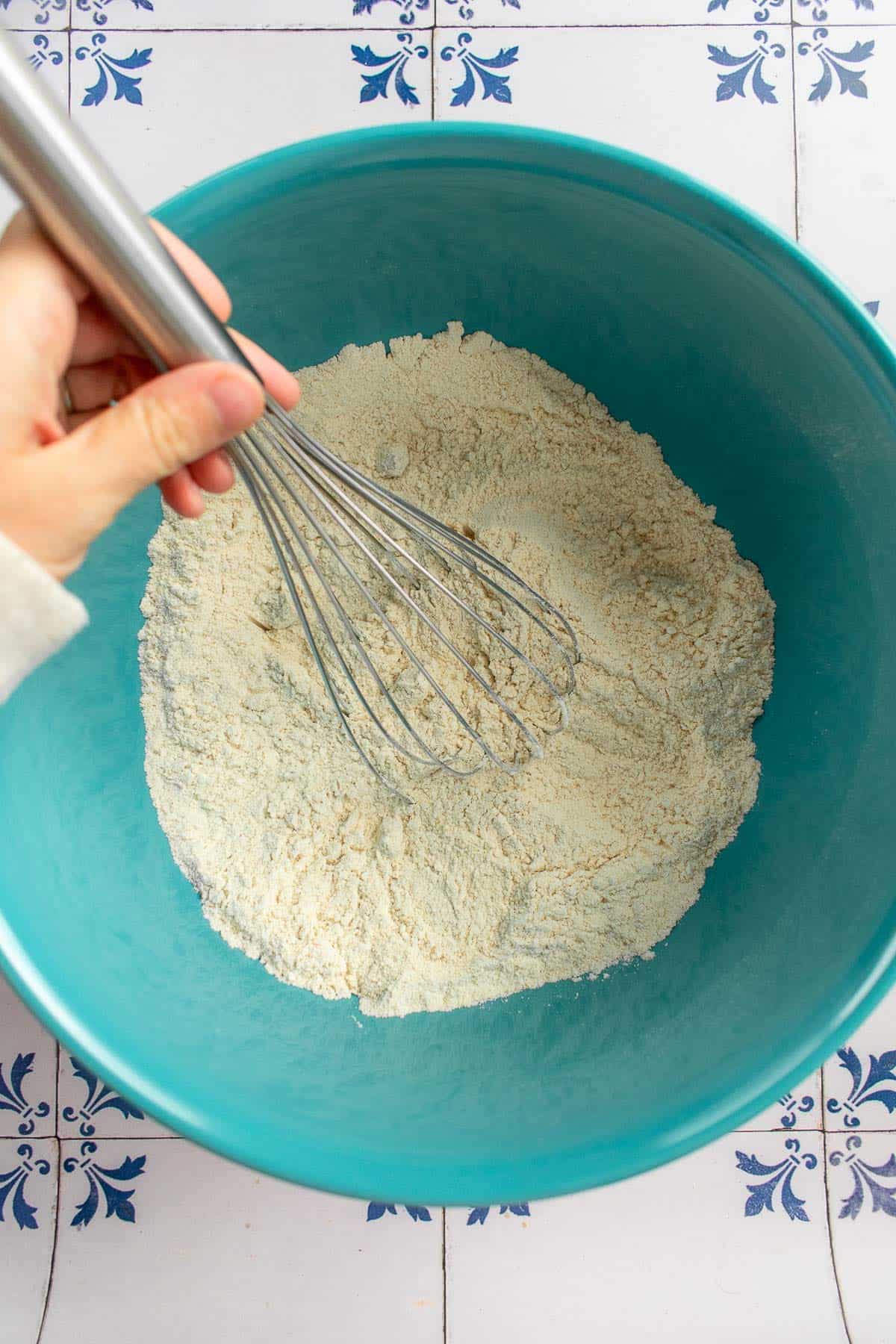 A hand whisking flour in a blue bowl.