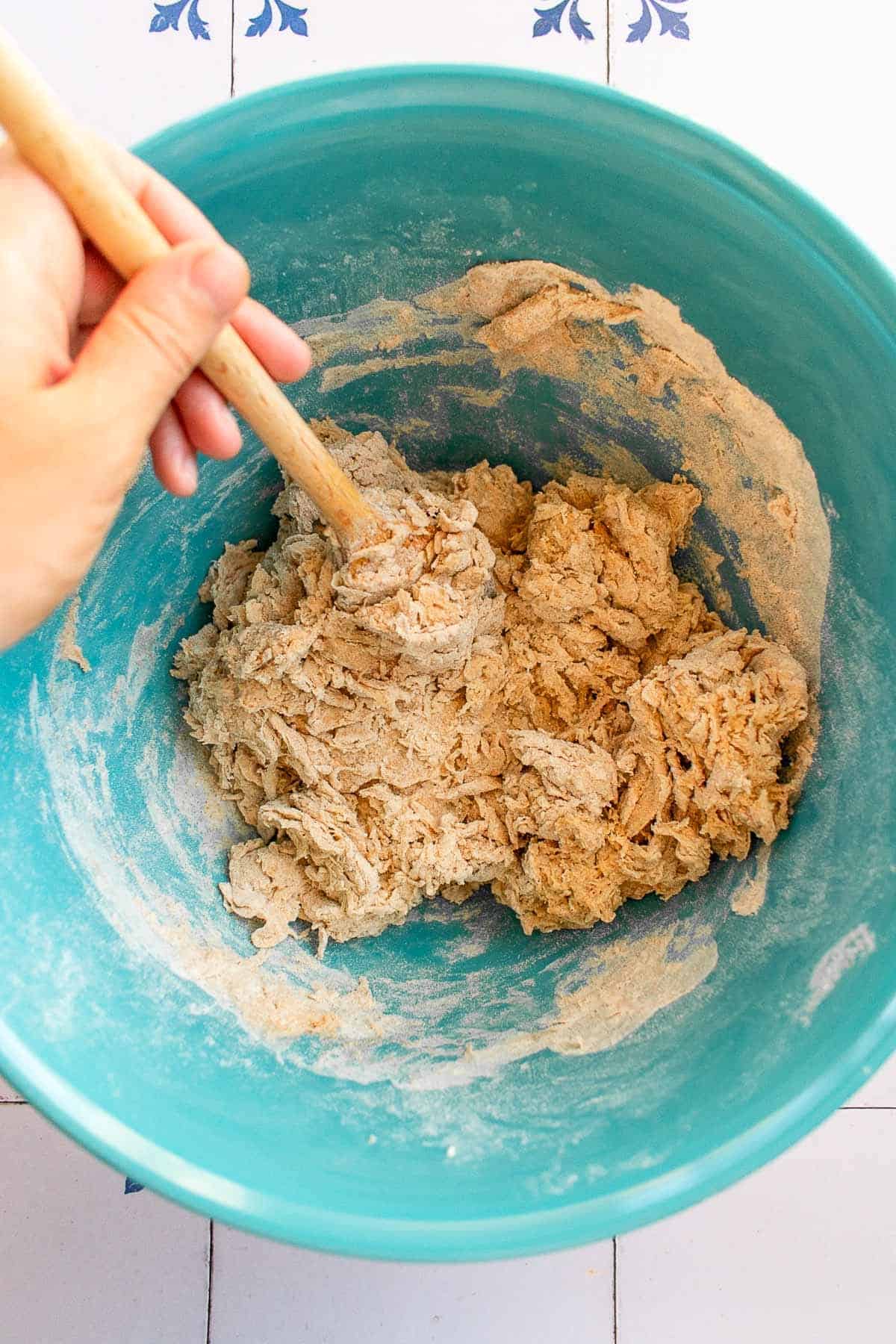 A hand mixing dense bread dough in a bowl. 