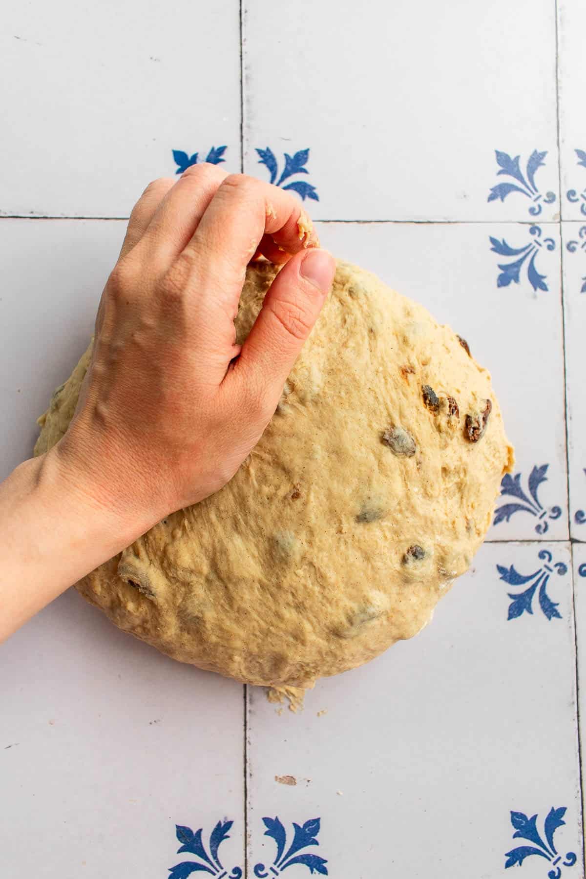 A hand kneading a ball of raisin bread dough on a table.