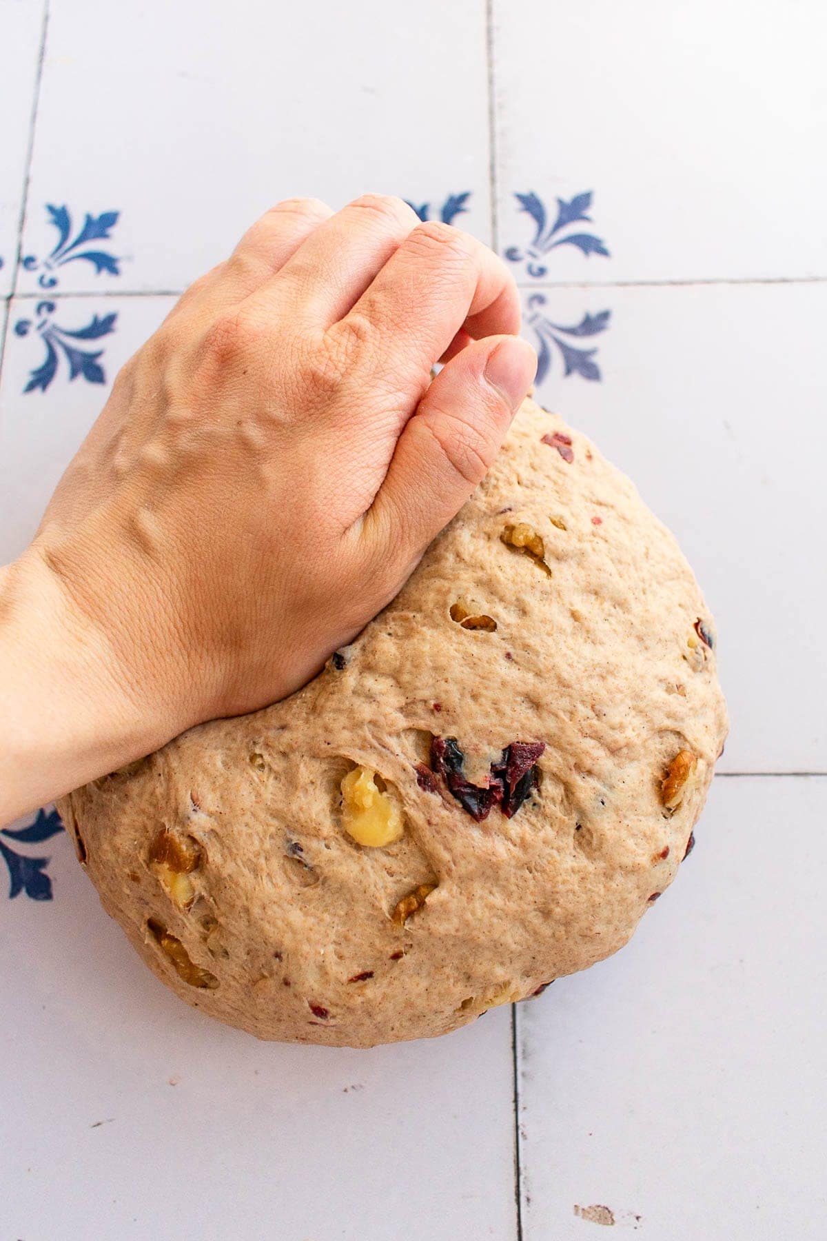 A hand kneading cranberry walnut bread dough on a table. 