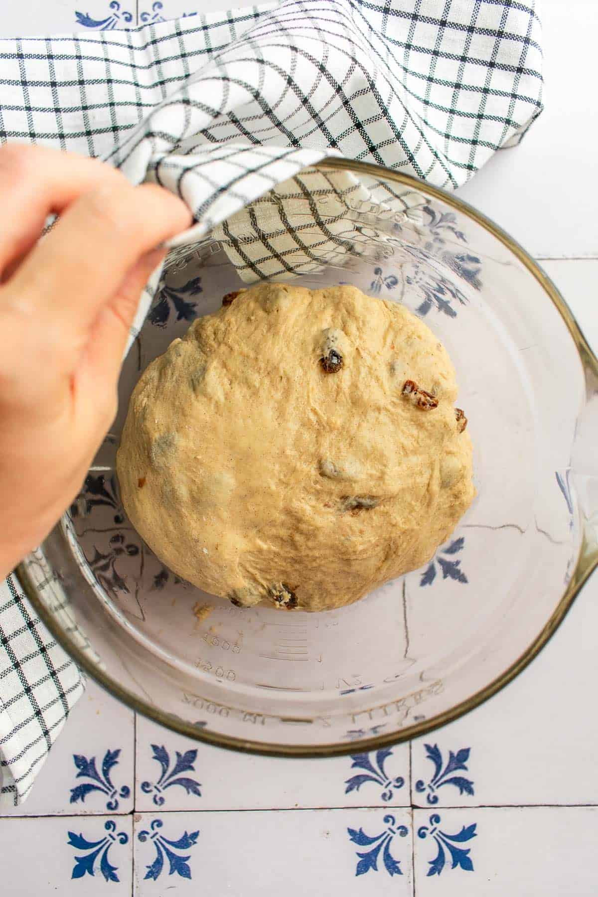 A hand covering a ball of dough in a bowl with a towel.