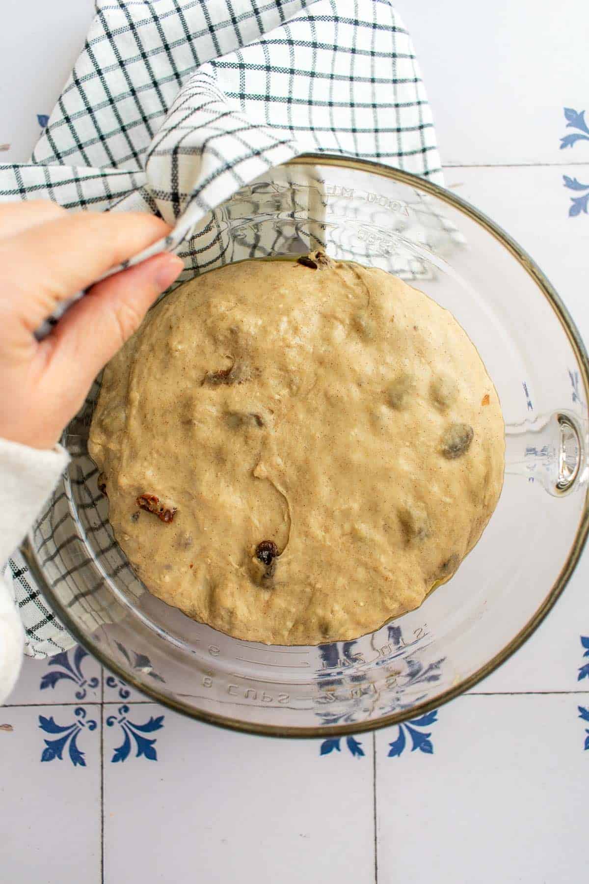A hand covering a risen ball of dough in a bowl with a towel.