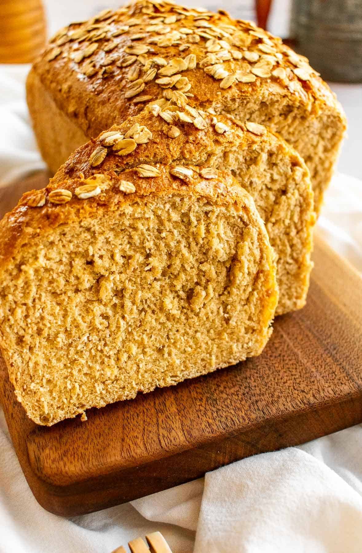 Slices of bread topped with honey and oats on a cutting board.