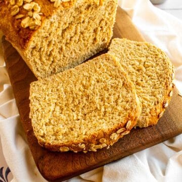 Two slices of honey oat bread next to the rest of the loaf.