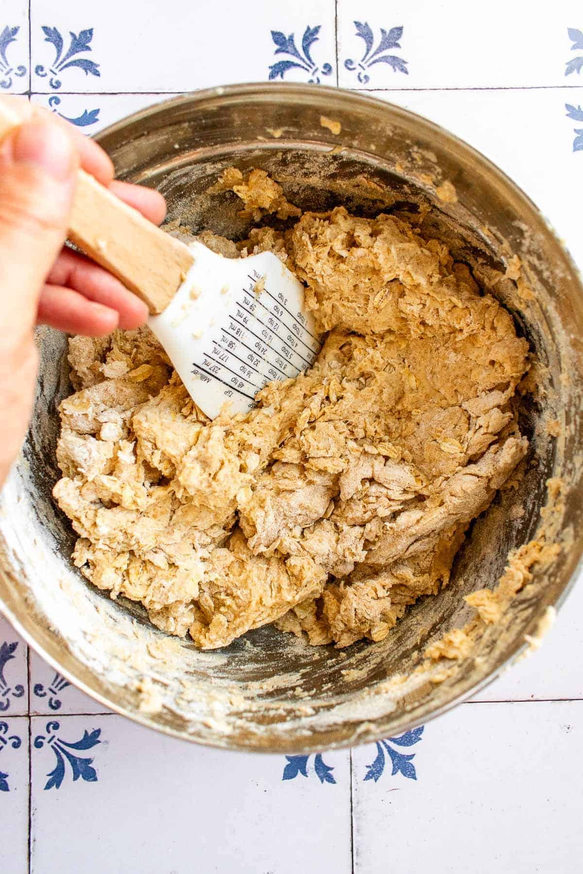 A hand mixing bread dough in a bowl with a spatula. 