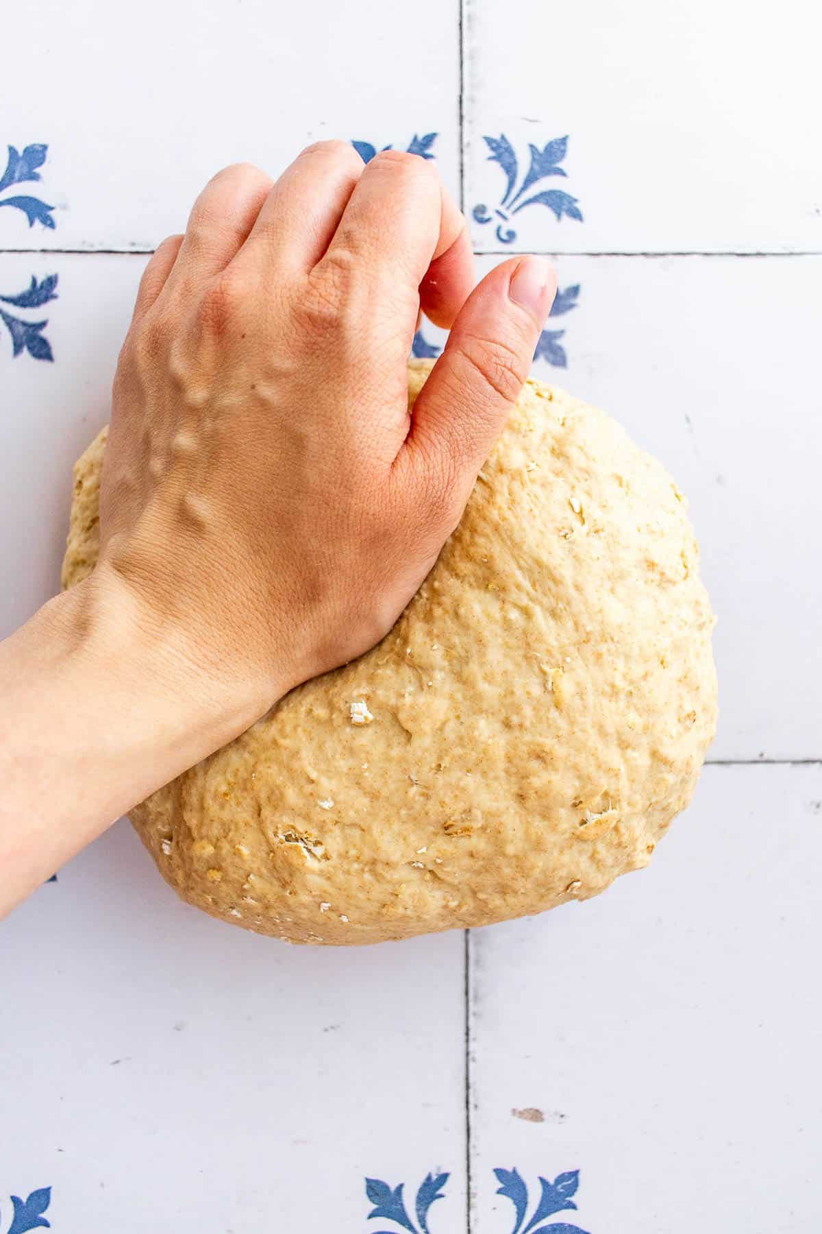 A hand kneading a ball of bread dough on a table. 