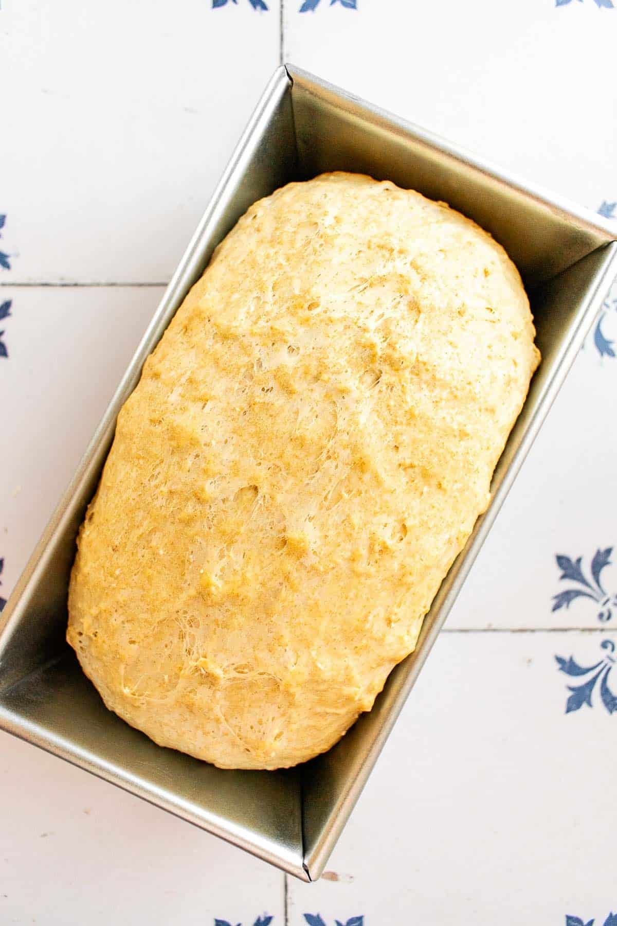 A loaf of proofed honey oat bread in a metal loaf pan.