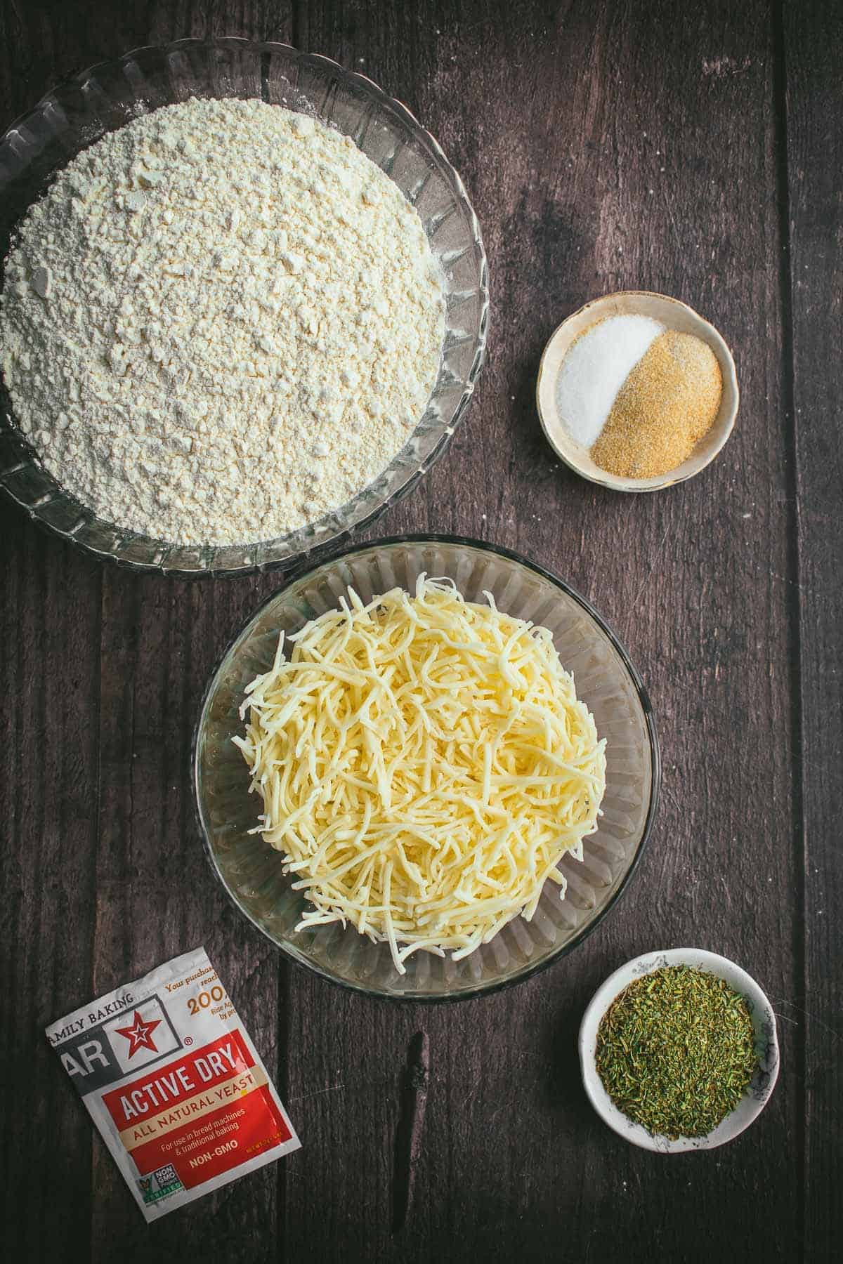 Bowls of flour, spices, cheese, and yeast on a table.