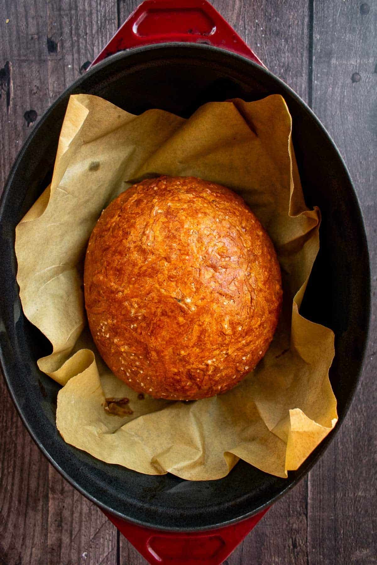 A baked loaf of Italian herb and cheese bread in a Dutch oven.