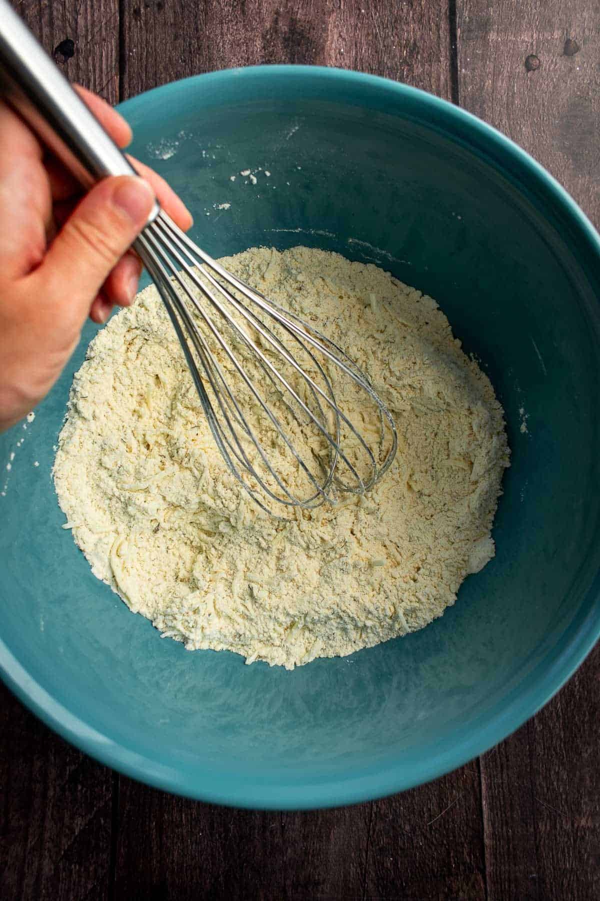 A hand whisking flour in a blue bowl.