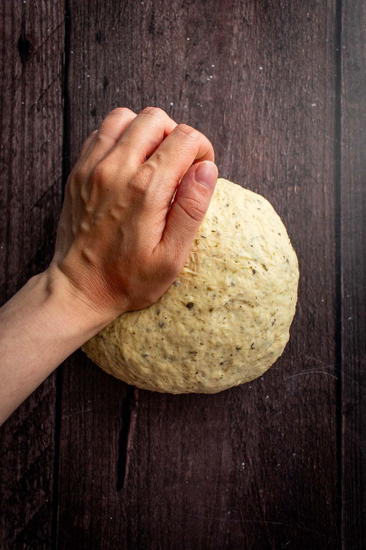 A hand kneading dough on a wood table.