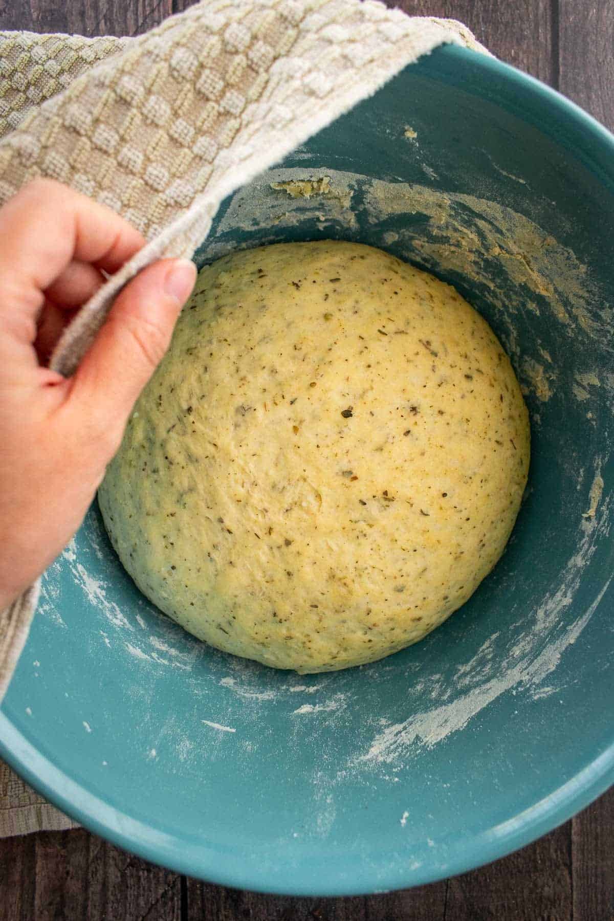 A large ball of risen herb bread dough in a mixing bowl.