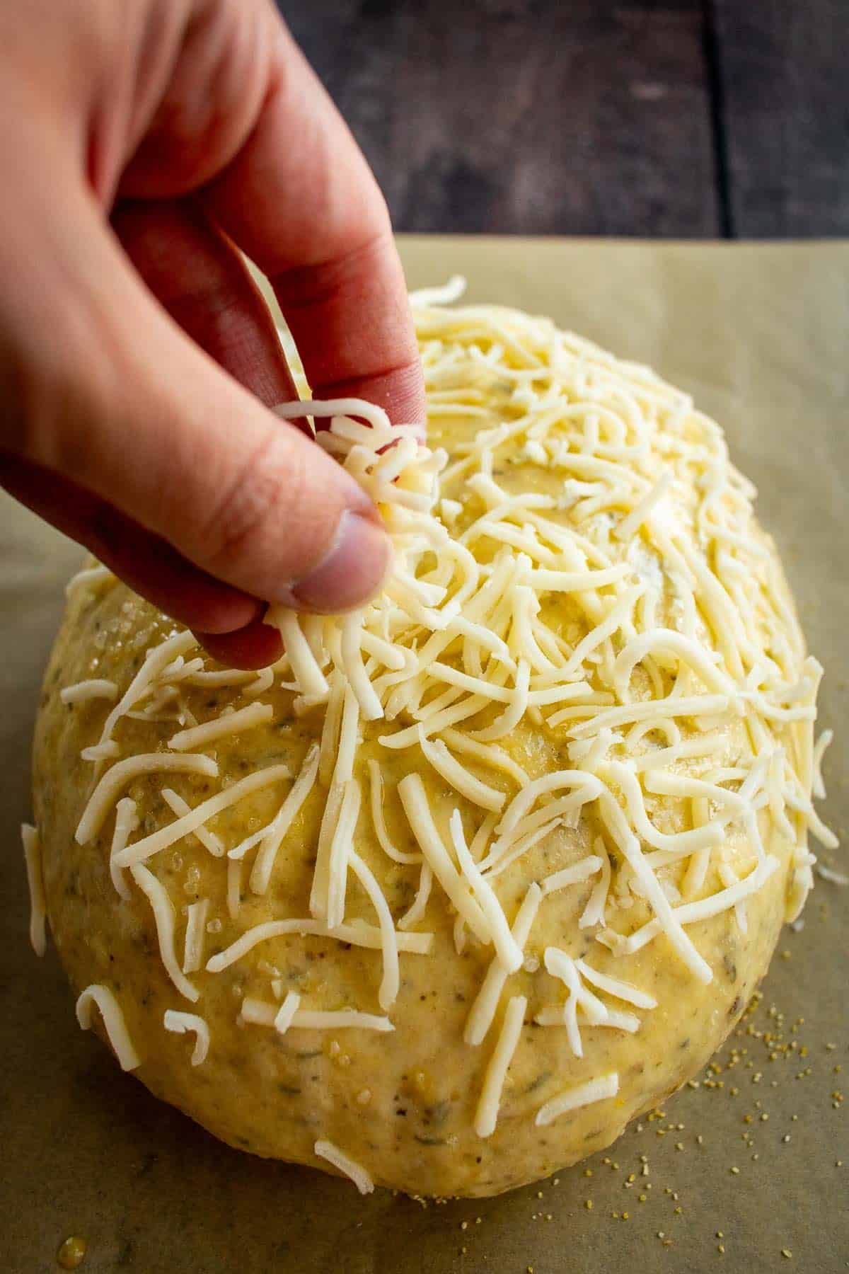 A hand sprinkling cheese on top of a loaf of unbaked bread.