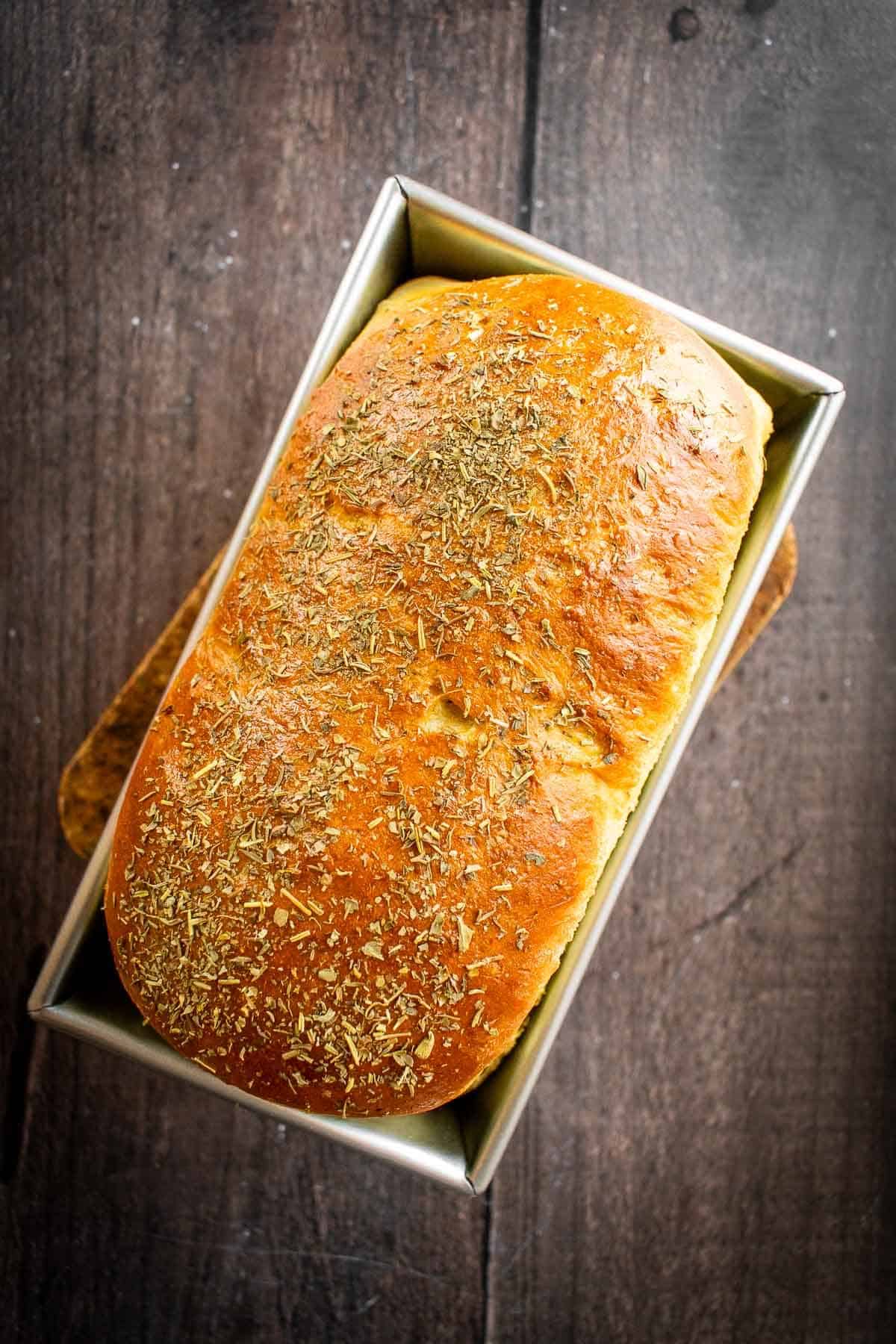 A loaf of baked bread in a metal loaf tin.