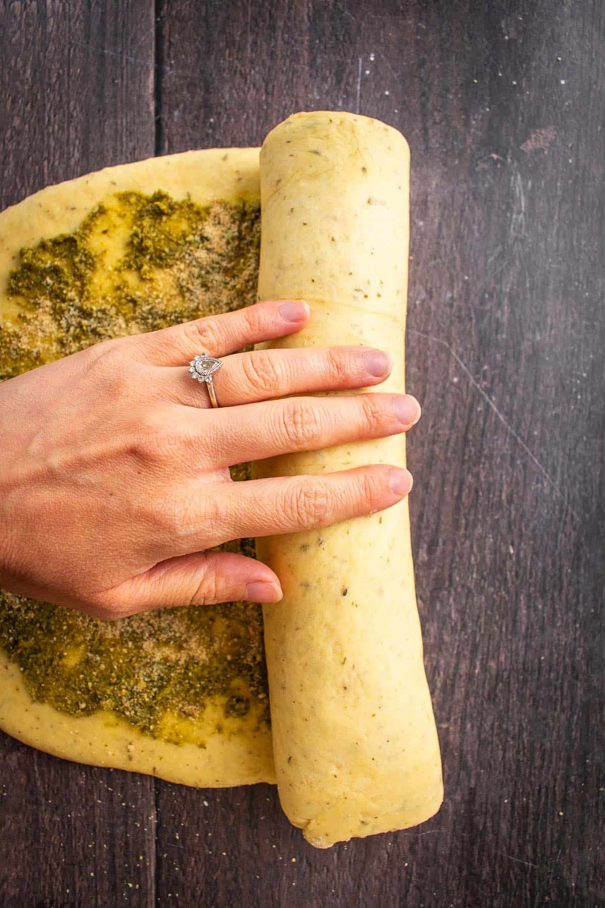 A hand rolling up a log of yeast bread dough.