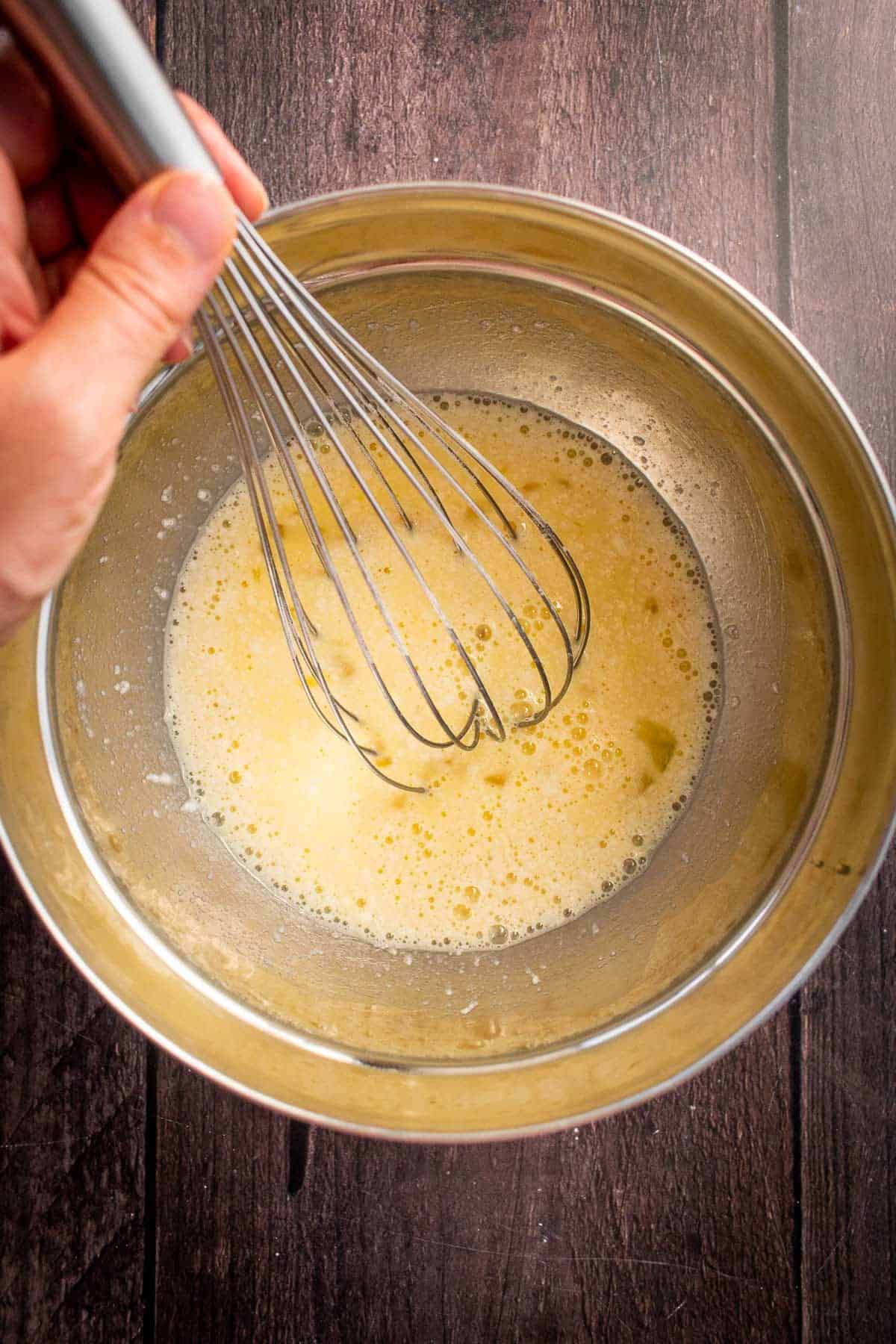 A hand whisking a wet, yellow mixing in a bowl.