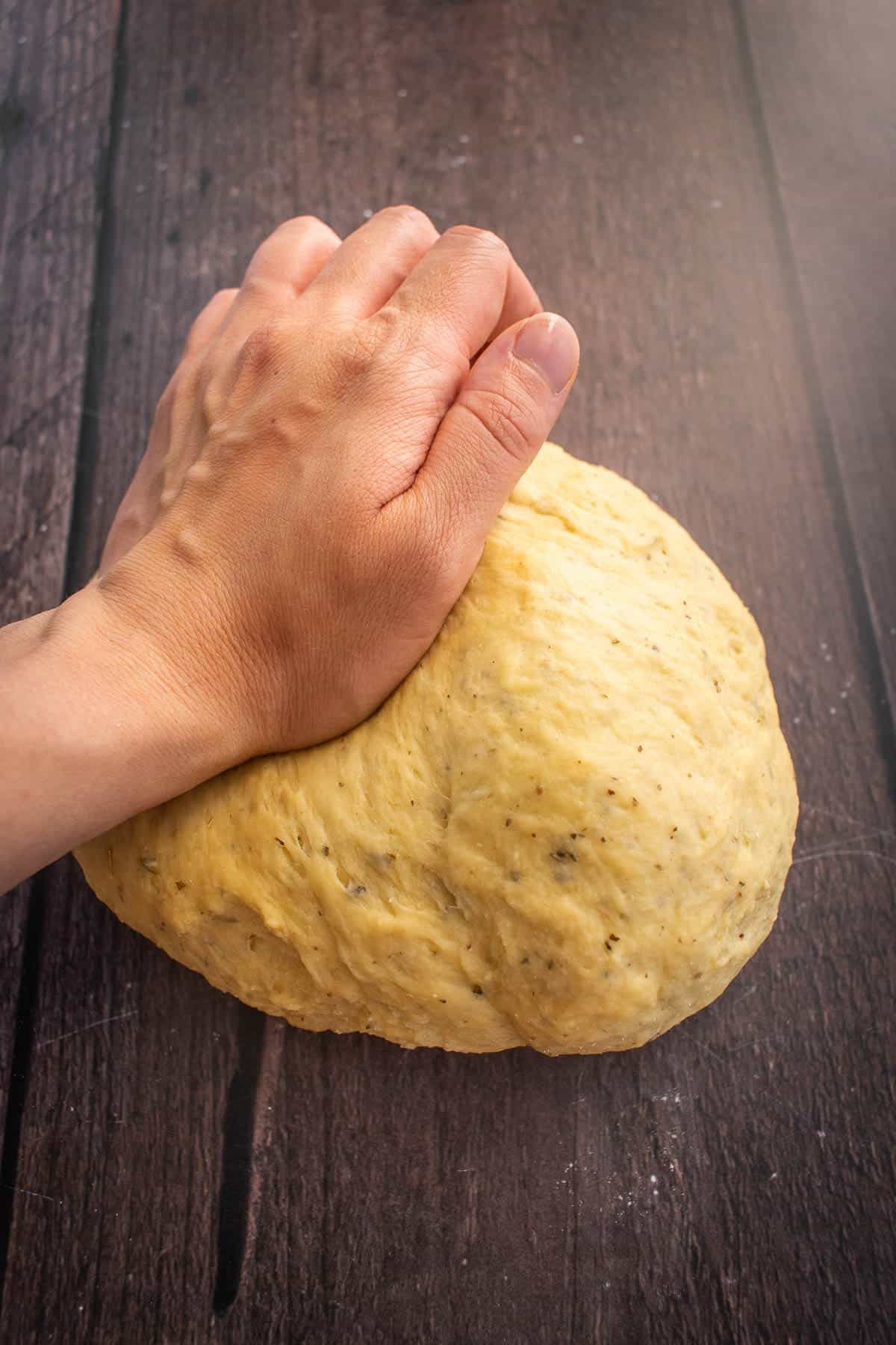 A hand kneading bread dough on a wooden table.
